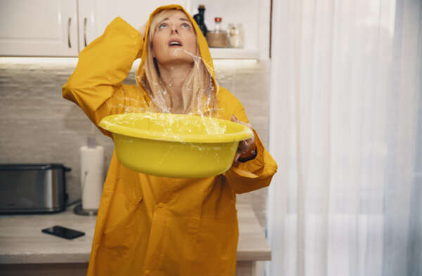 Woman in yellow raincoat looking at Water Leak From the Ceiling. Home flooded by roof damage or broken pipe. Copy space